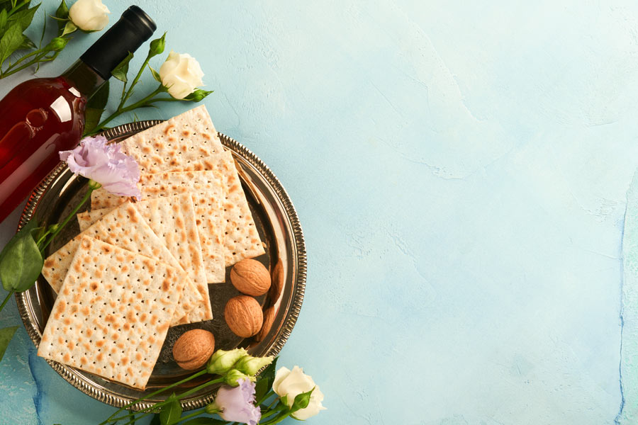 Photo of flowers, wine, matzo, and nuts on light blue textured background